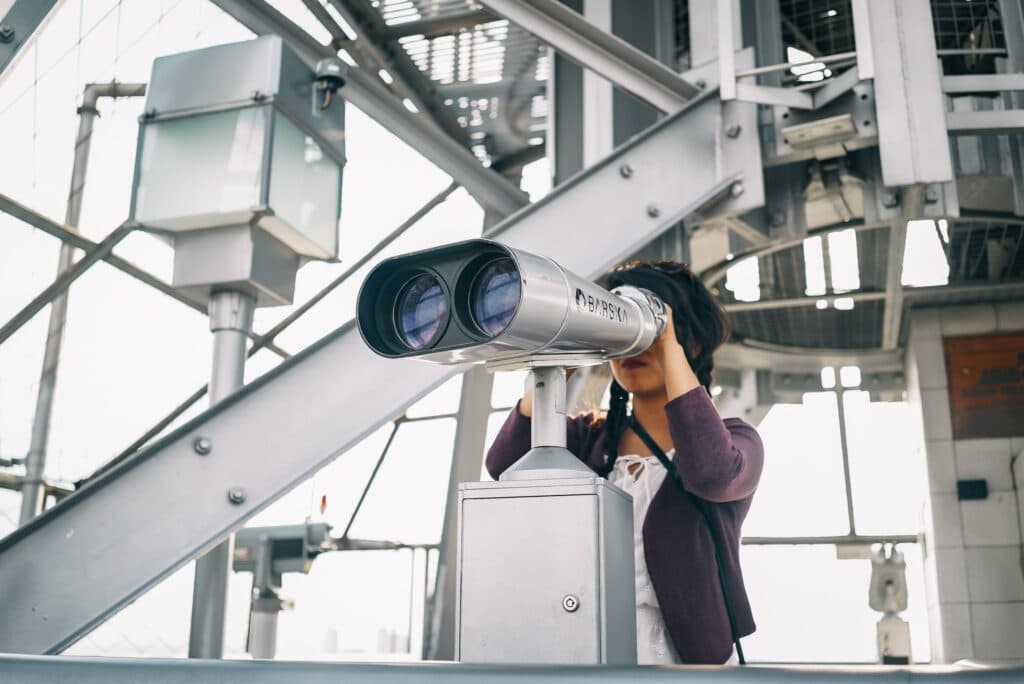 A person looking through a viewing scope inside an airy industrial hall